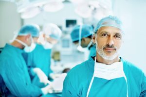 Portrait of senior doctor smiling in the operating theater with team performing surgery in background